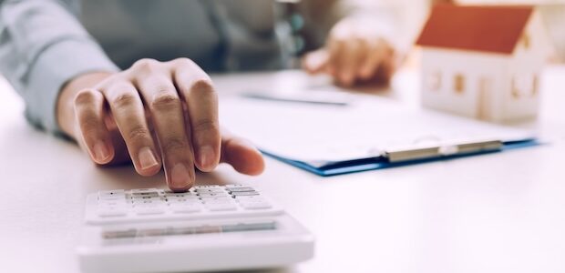 Person berechnet mit Taschenrechner die Umschuldung für einen Hauskredit AB