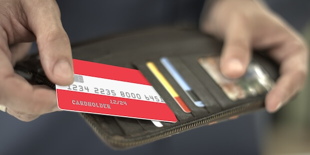 Mann sortiert Kreditkarte mit Farben, die für die Österreich-Flagge stehen, in die Geldbörse ein - Symbolbild für Gratis-Kreditkarten für Österreich AB