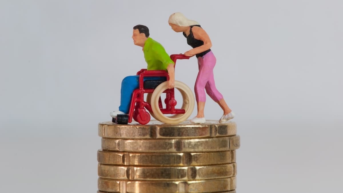 Berufsunfähigkeitsversicherung berechnen: Miniaturfigur schiebt eine Person im Rollstuhl auf einem Stapel Münzen